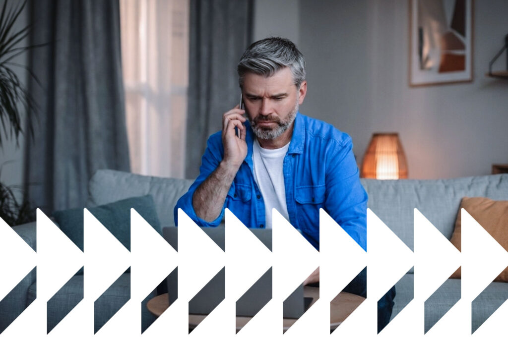 A imagem mostra um homem falando ao telefone enquanto utiliza um computador.